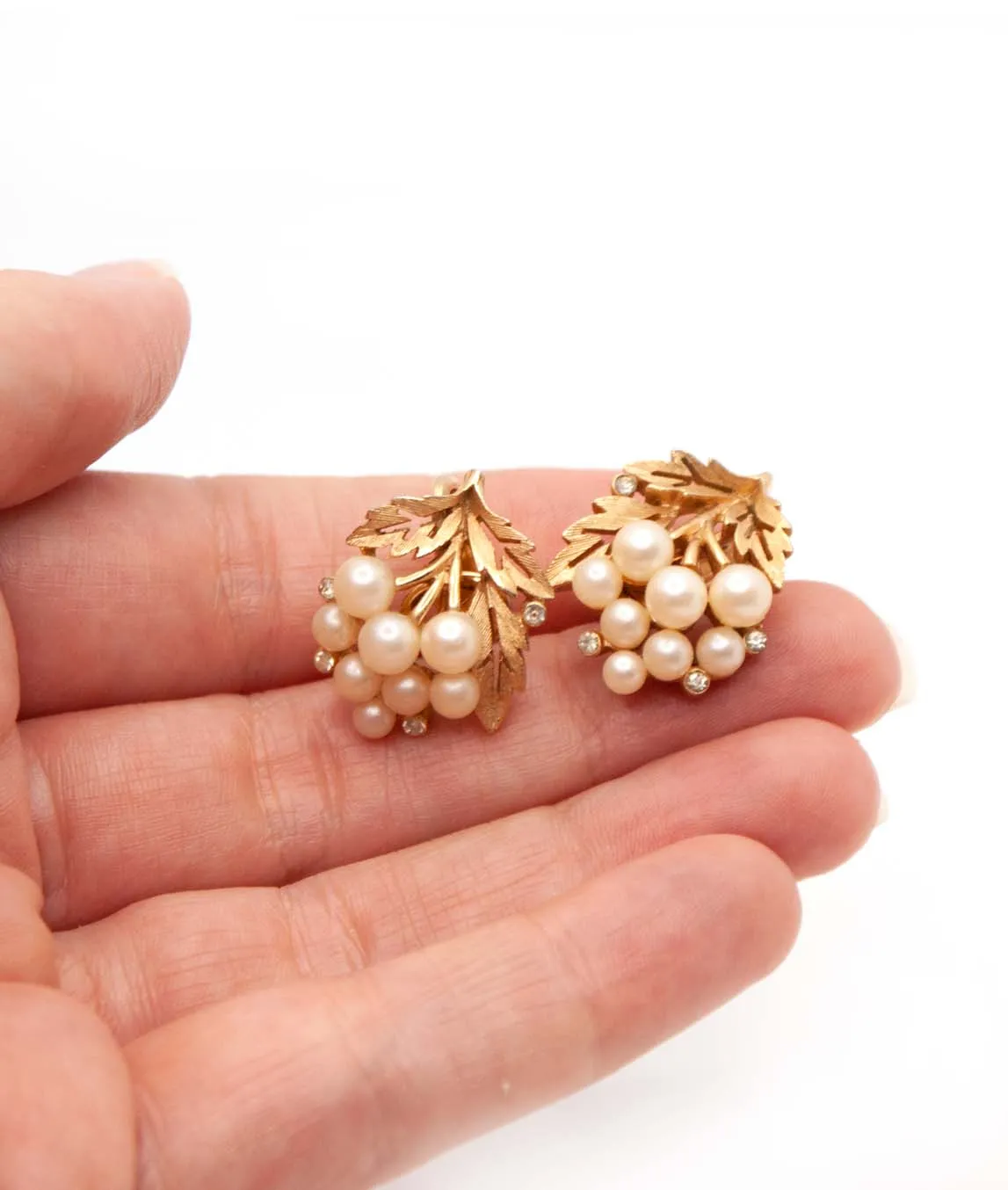 Crown Trifari textured gold plated earrings with faux pearls and rhinestones in a hand